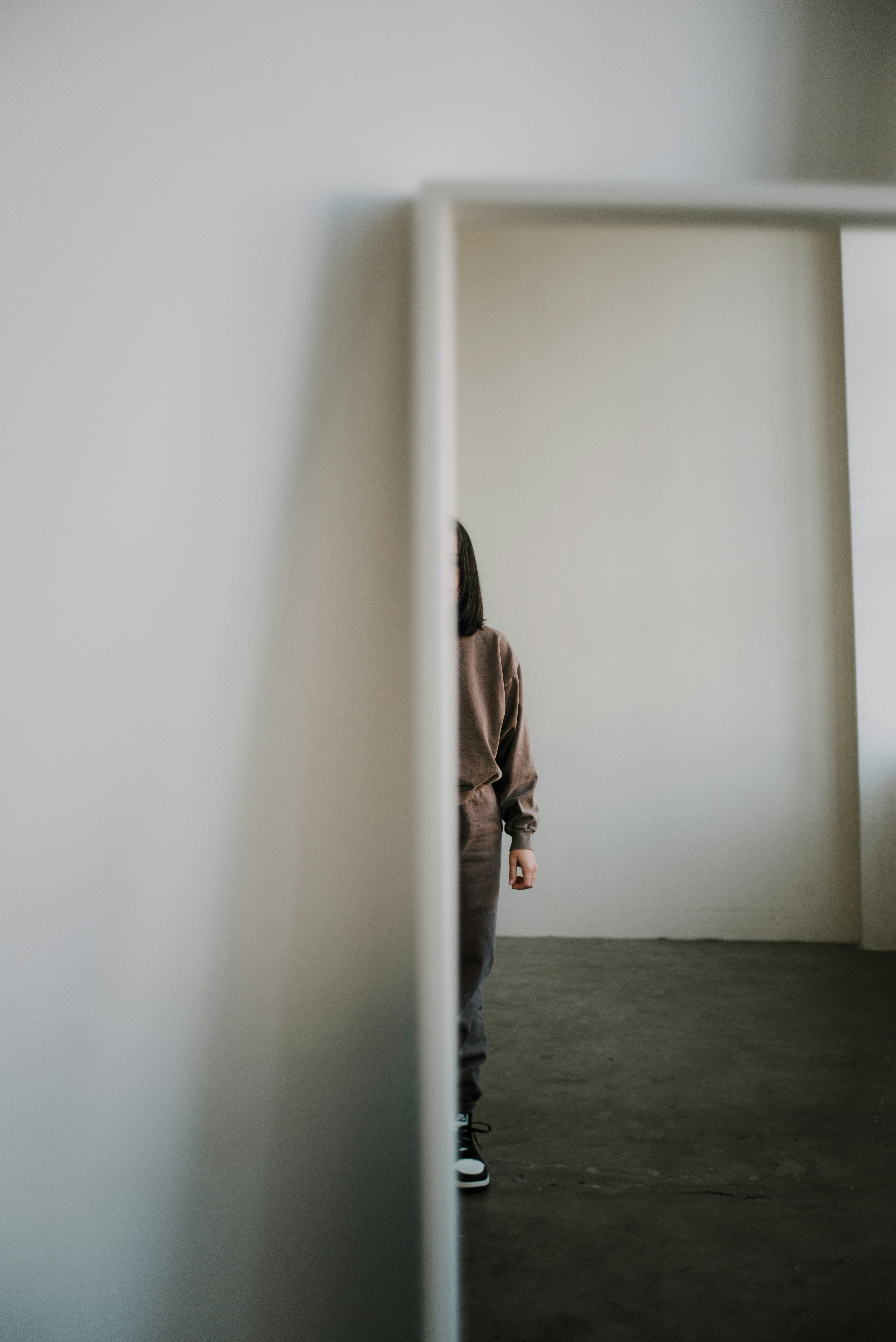 woman in brown jacket and black pants standing beside white wall